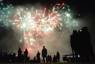 Silhouettes of audience members watching white and red fireworks