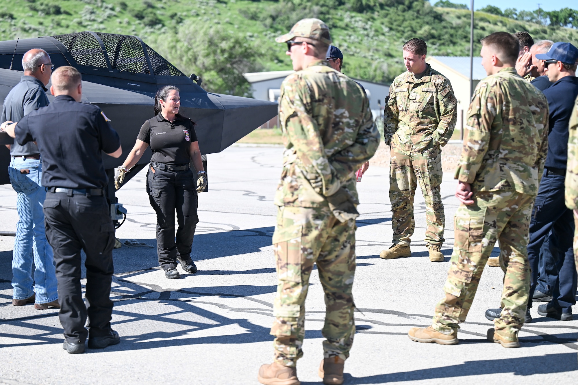 military personnel and civilians gathered around a fire training airplane prop outdoors for training