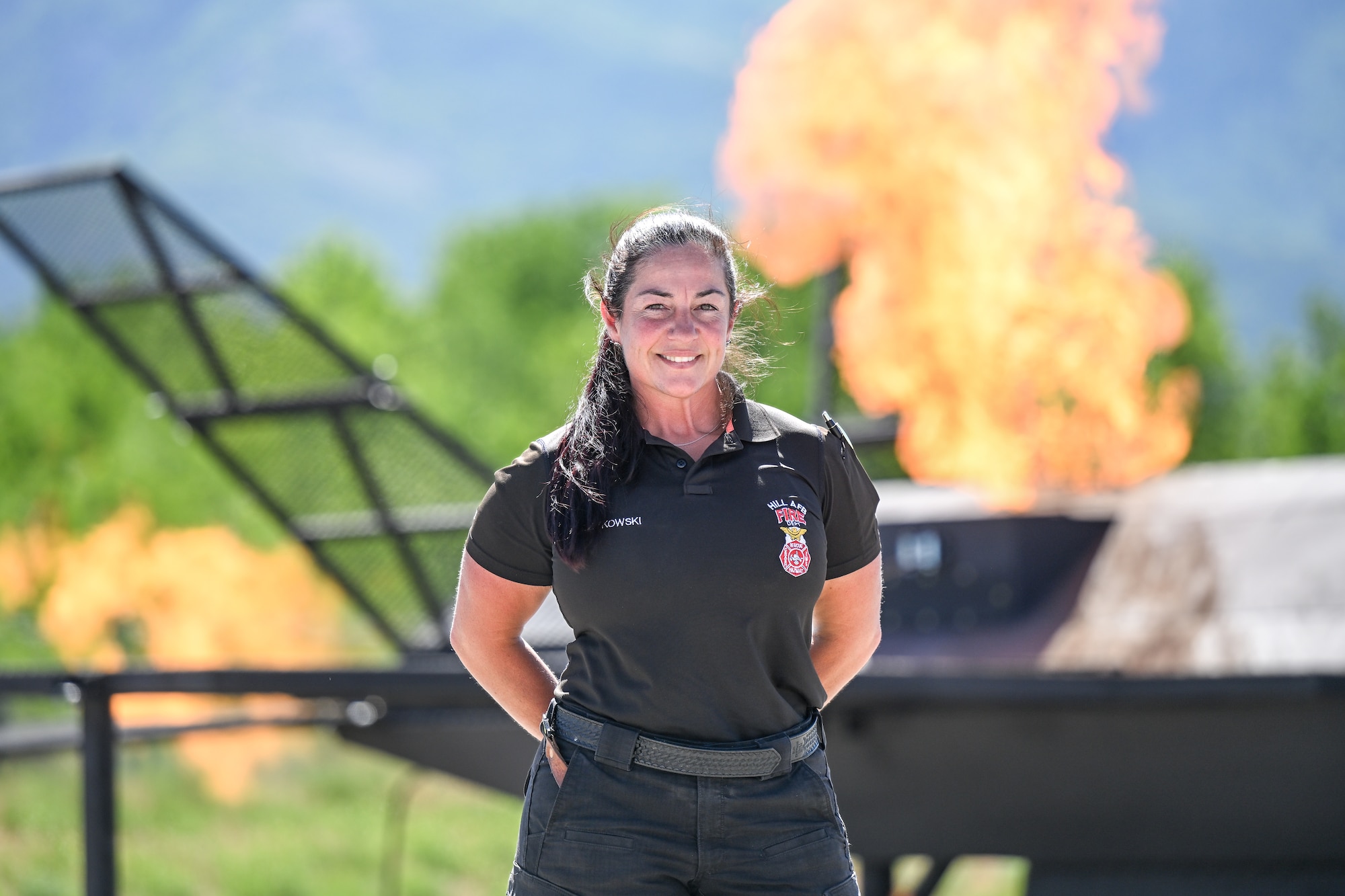 Female firefighter smiling with large flames burning from a plane prop in the background
