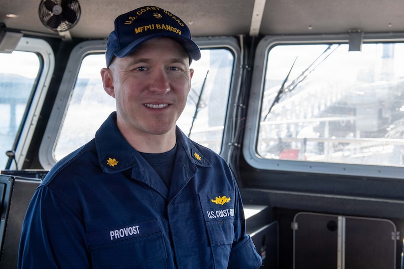 A coast guardsman in a blue uniform smiles inside a vessel.