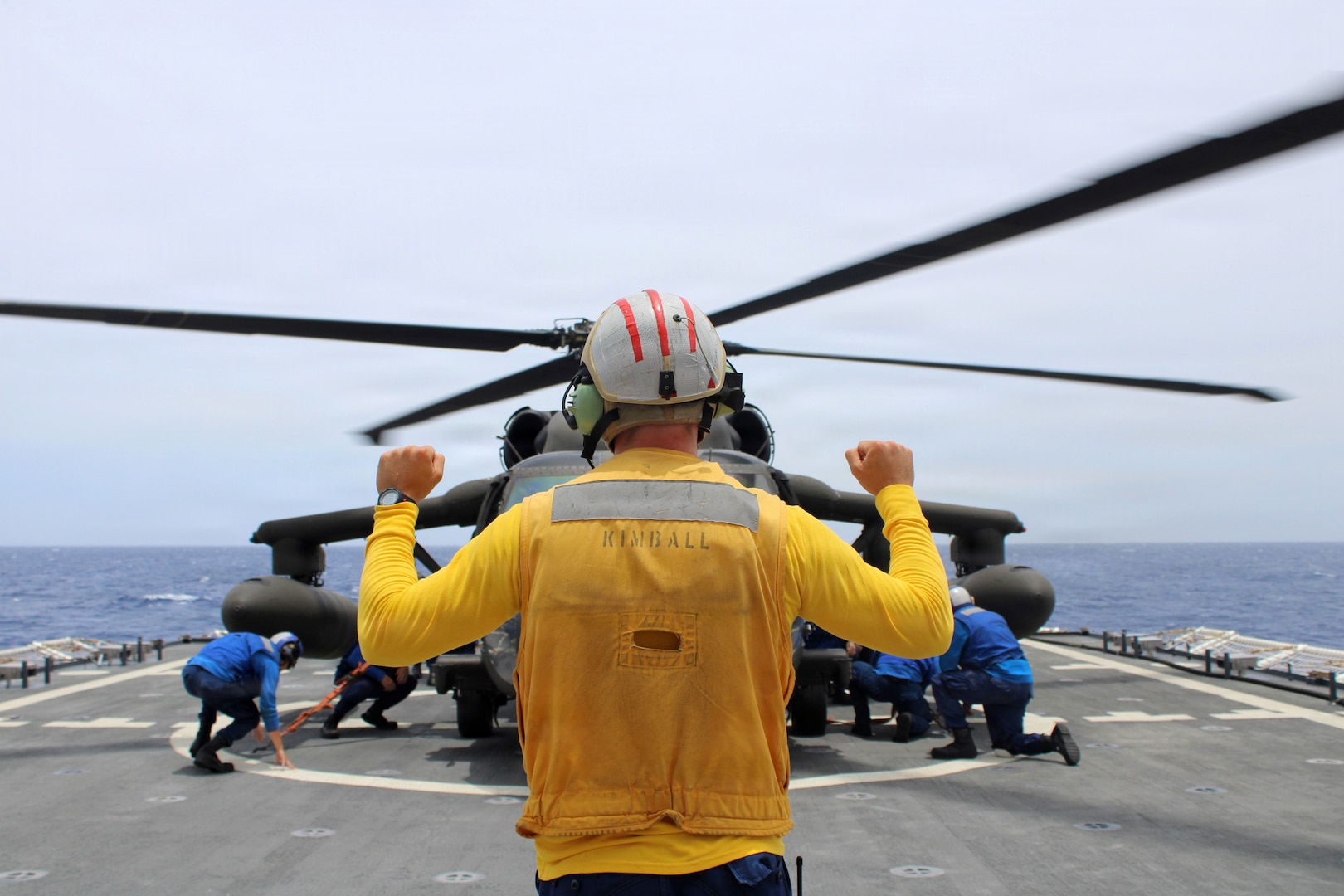 A landing signal officer aboard the Legend-class national security cutter USCGC Kimball (WMSL 756) directs the cutter’s tiedown team using hand signals during helicopter training with a U.S. Army MH-60 while patrolling off the coast of Honduras June 2, 2026. Joint training opportunities enhance interoperability between the services and support preparedness for humanitarian assistance and disaster relief operations at the start of hurricane season. (U.S. Coast Guard photo by Petty Officer 2nd Class Emigdio Virgen).