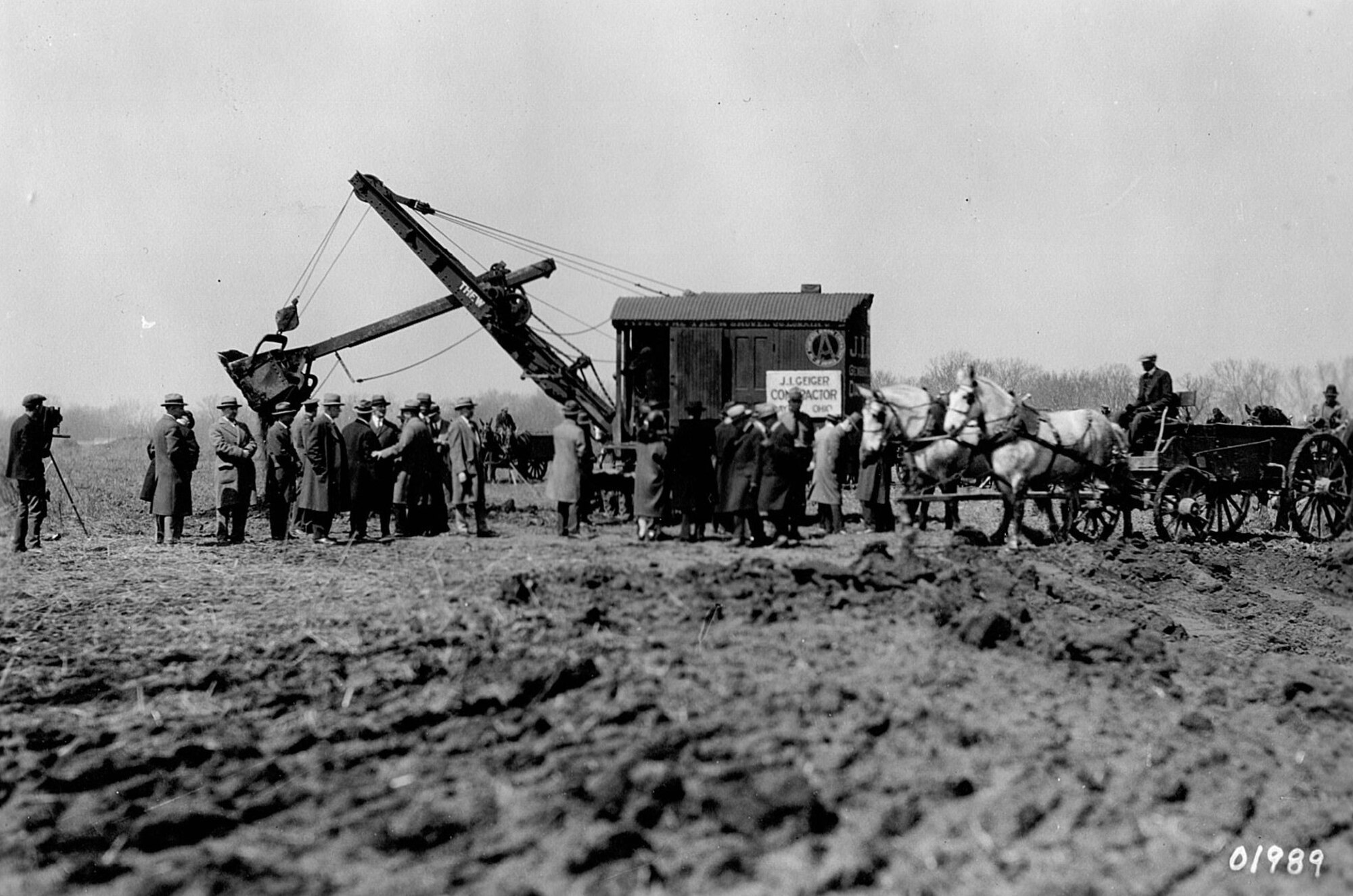 A machine being used to break ground with people in attendance watching.