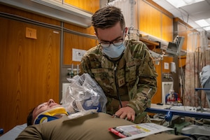 An Airman wearing a mask listens to a patients heartbeat.