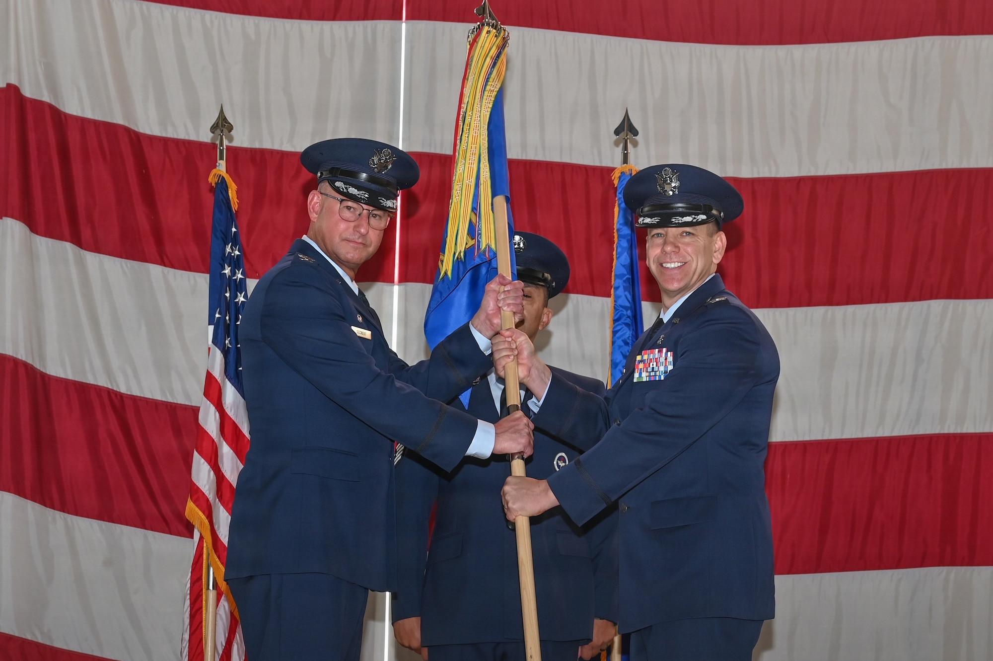 U.S. Air Force Col. Cody J. Hess, incoming Kirtland Medical Group commander, right, receives the guidon from Col. Justin D. Secrest, 377th Air Base Wing and installation commander, left, during the Kirtland Medical Group change of command ceremony at Kirtland Air Force Base.