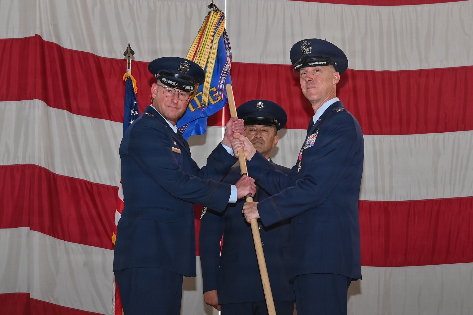 U.S. Air Force Col. Steven M. Fox, outgoing Kirtland Medical Group commander, right, passes the guidon to Col. Justin D. Secrest, 377th Air Base Wing and installation commander, left, during the Kirtland Medical Group change of command ceremony at Kirtland Air Force Base.