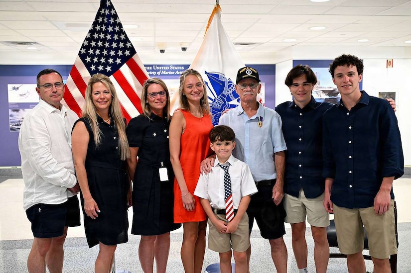 Eight people pose for a photo in front of an American flag and an Army flag.