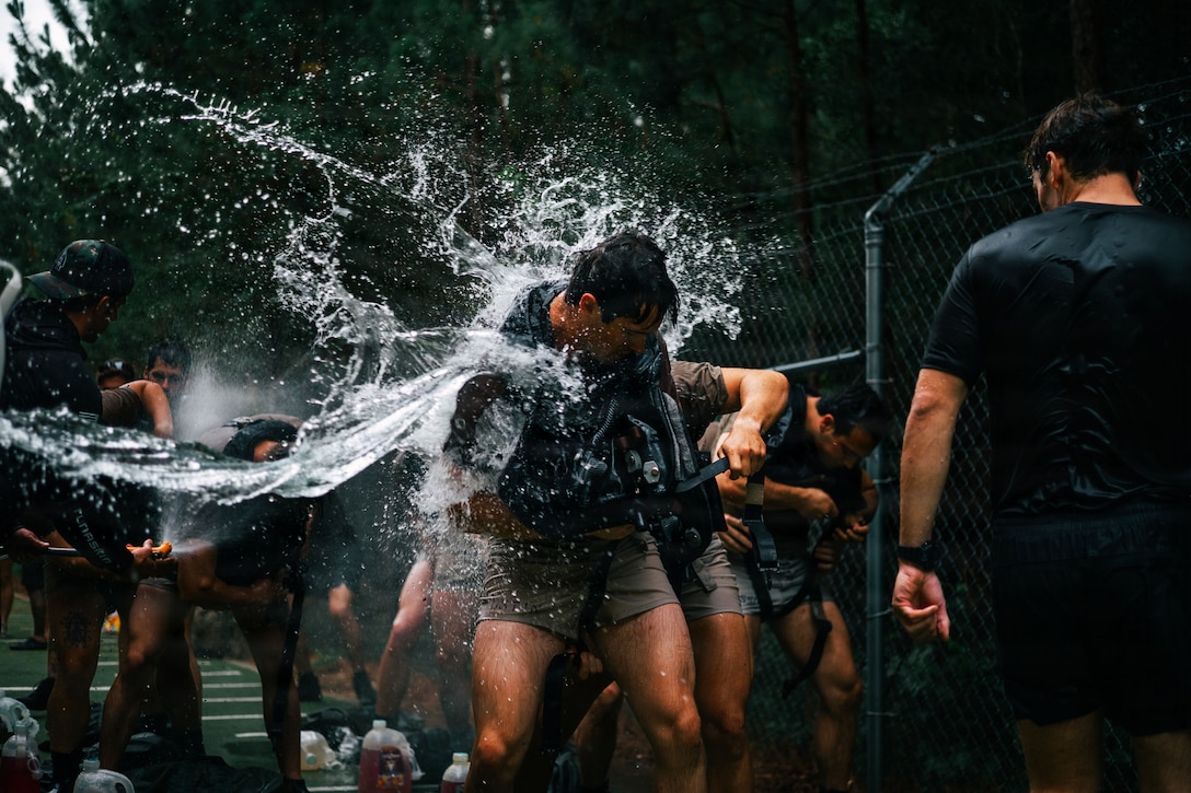 Soldiers in athletic attire are splashed with water outside.