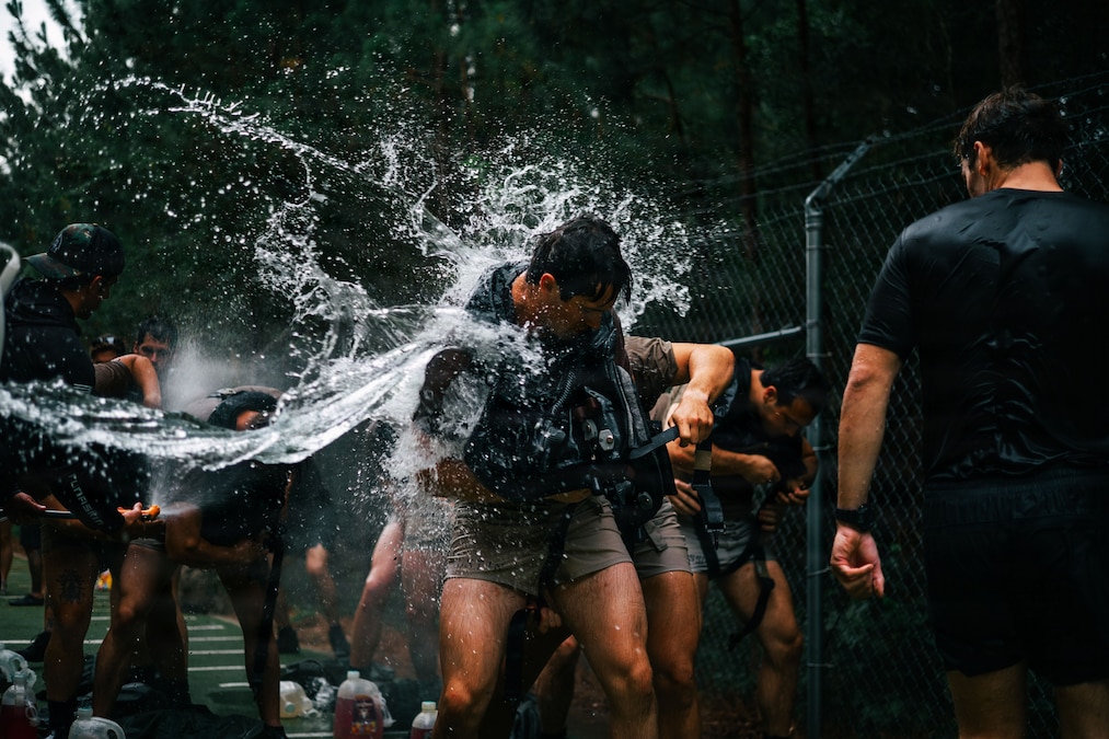 Soldiers in athletic attire are splashed with water outside.