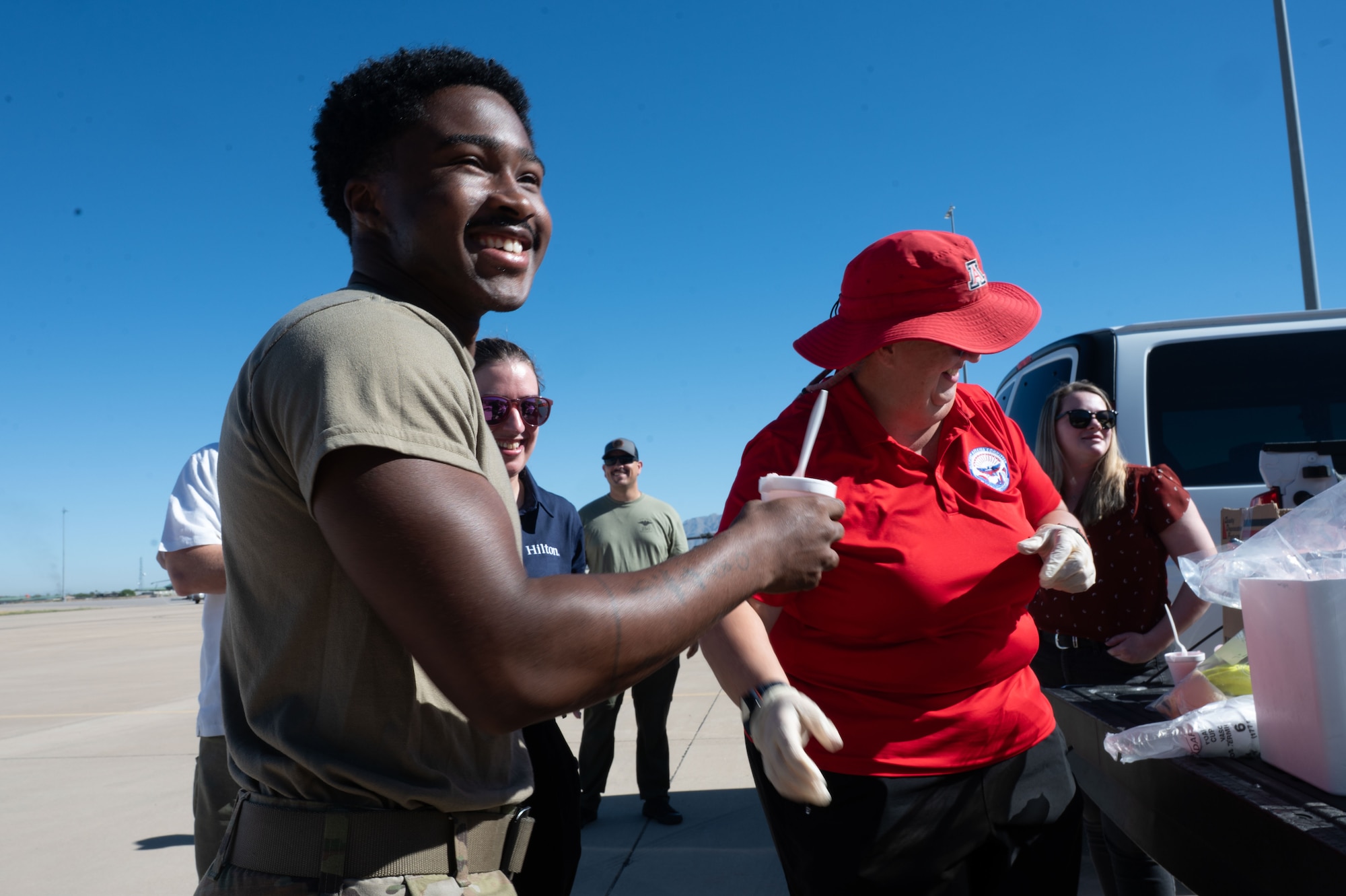 U.S. Airman receives shaved ice from a DM50 member on the flightline at Davis-Monthan Air Force Base, Arizona, July 2, 2026. DM50, the Military Affairs Committee and base first sergeants aimed to boost morale and show appreciation for Airmen enduring high temperatures on the flight line and in other outdoor areas by handing out shaved ice. (U.S. Air Force photo by Airman 1st Class Jaden Kidd)