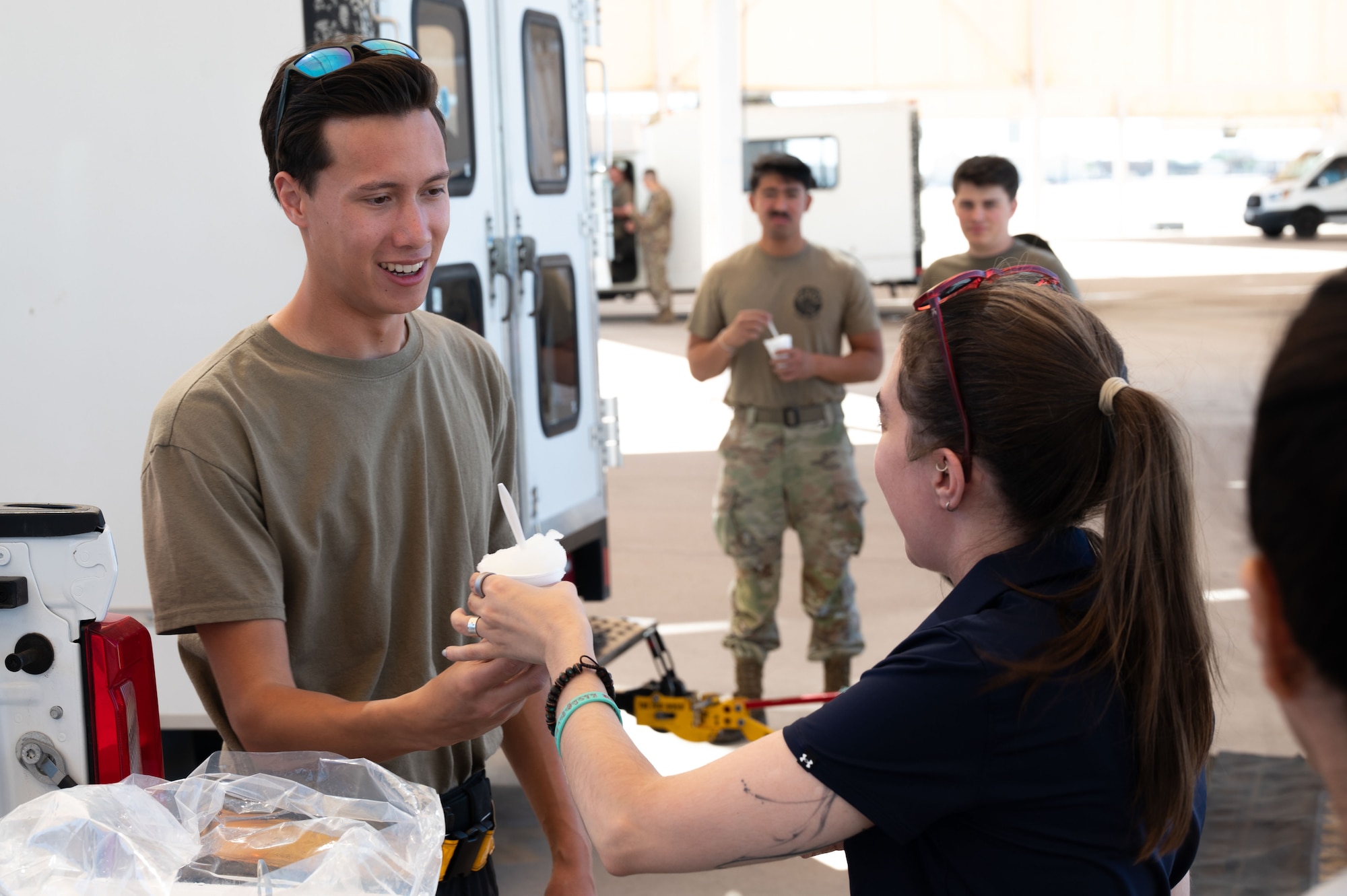 A DM50 member, hands shaved ice to an Airman at Davis-Monthan Air Force Base, Arizona, July 2, 2026. DM50, the Military Affairs Committee and base first sergeants aimed to boost morale and show appreciation for Airmen enduring high temperatures on the flight line and in other outdoor areas by handing out shaved ice. (U.S. Air Force photo by Airman 1st Class Jaden Kidd)