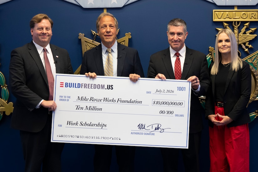 Four people stand near one another and hold a large paper check written for $10 million.
