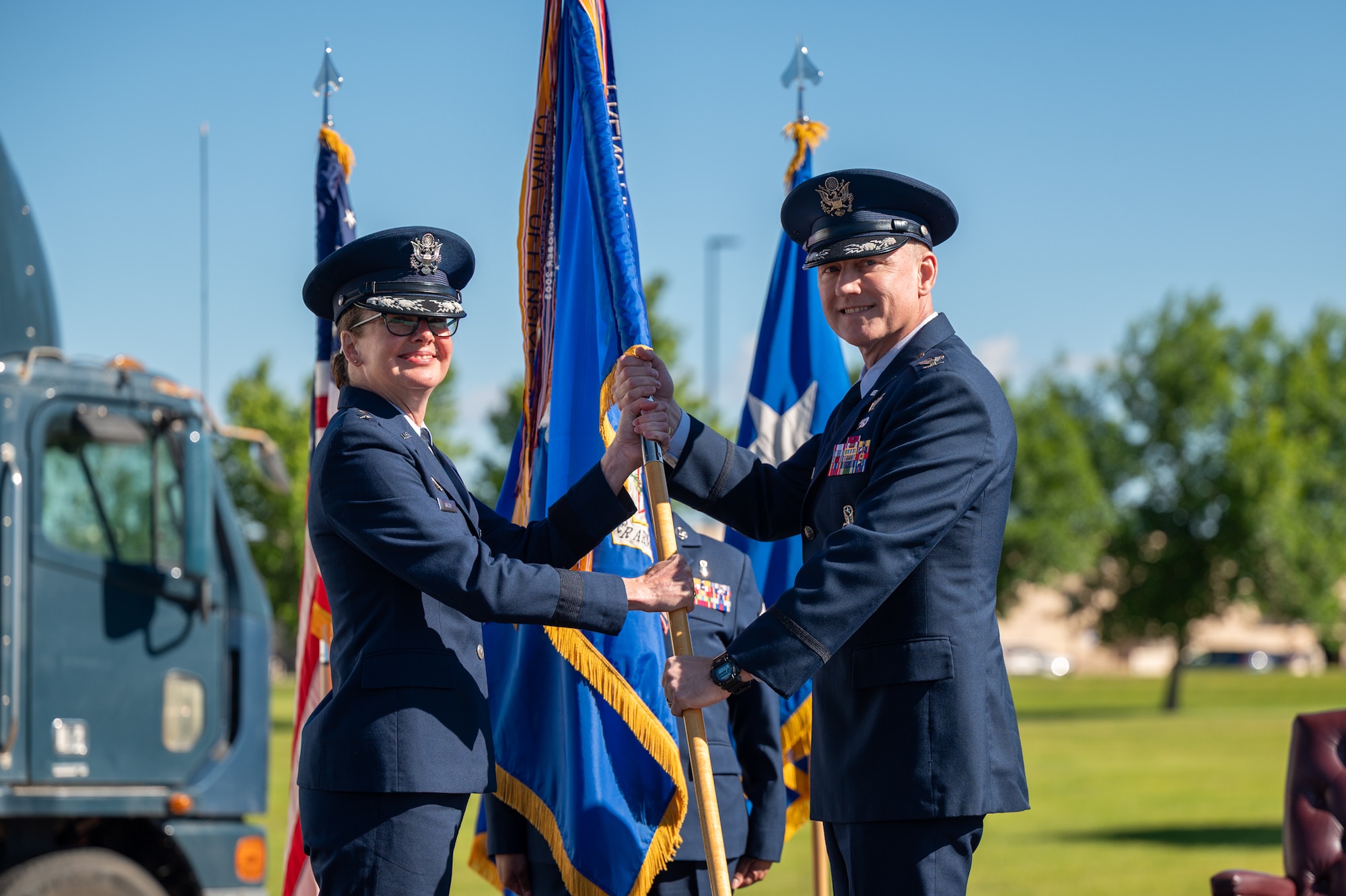 Two uniformed personnel smile for a photo while holding a guidon.