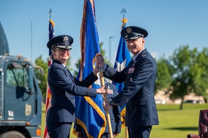 Two uniformed personnel smile for a photo while holding a guidon.