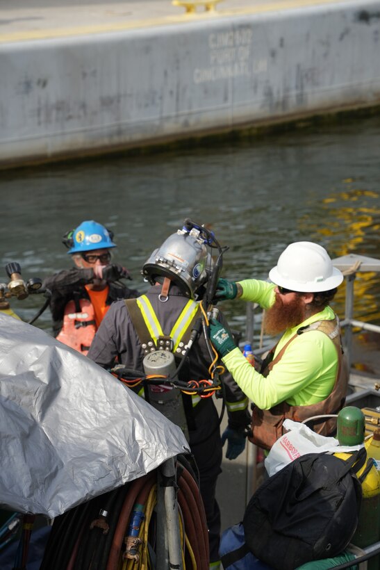 A dive team member helps a diver conduct final equipment checks before an underwater inspection at the Chickamauga Lock Replacement Project site in Chattanooga, Tenn., June 16, 2026. Divers perform essential quality control by using feeler gauges to verify that each 420-ton concrete beam rests securely on its bearing pads. This meticulous process is crucial to the U.S. Army Corps of Engineers' mission of safely delivering modern and resilient infrastructure for the nation's inland waterways. (USACE Photo by Noe Gonzalez)