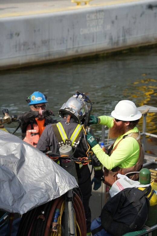 A dive team member helps a diver conduct final equipment checks before an underwater inspection at the Chickamauga Lock Replacement Project site in Chattanooga, Tenn., June 16, 2026. Divers perform essential quality control by using feeler gauges to verify that each 420-ton concrete beam rests securely on its bearing pads. This meticulous process is crucial to the U.S. Army Corps of Engineers' mission of safely delivering modern and resilient infrastructure for the nation's inland waterways. (USACE Photo by Noe Gonzalez)