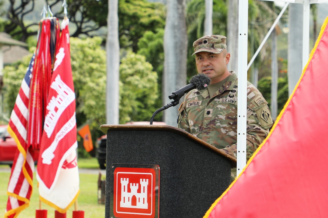A male soldier stands at a podium. There is a group of flags on a stand in the background.