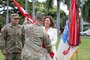 Back of a male Army Soldier is grasping a red flag wrapped around a pole from a smiling female in an off-white pants suit.