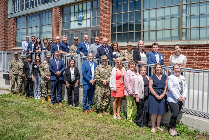 A large group photo of military and civilians posed outside a brick building along a railing