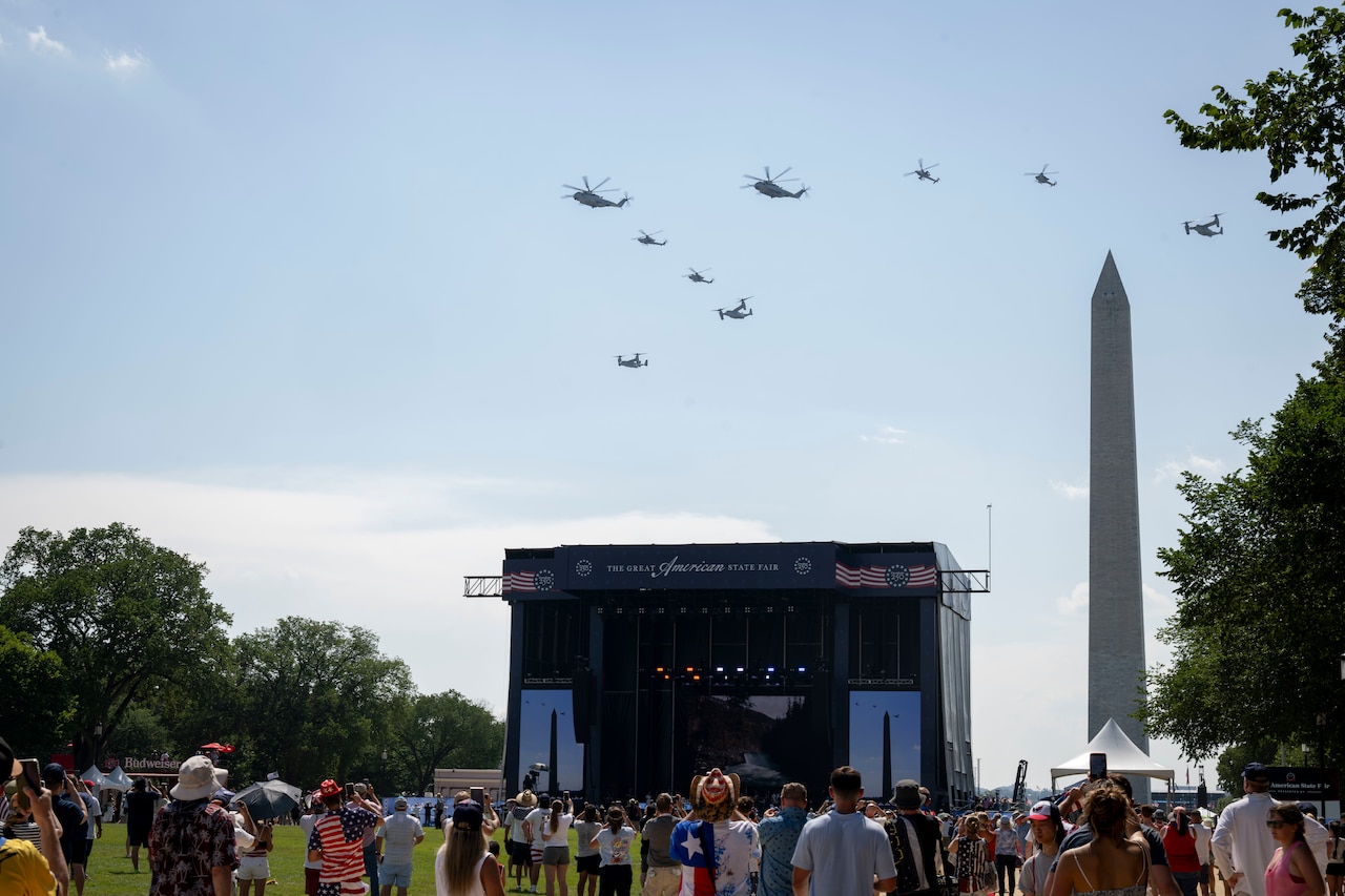 Helicopters fly over a stage and the Washington Monument.