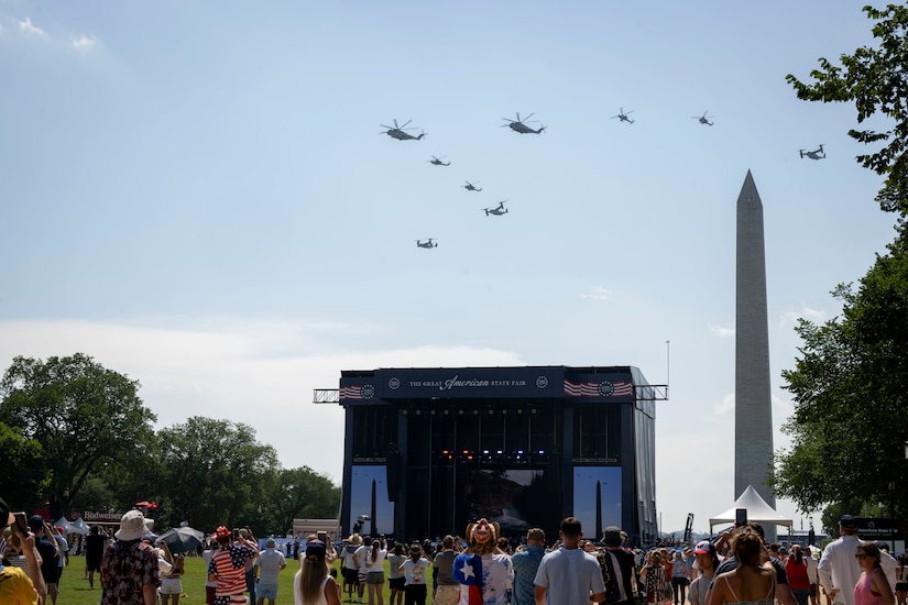Helicopters fly over a stage and the Washington Monument.