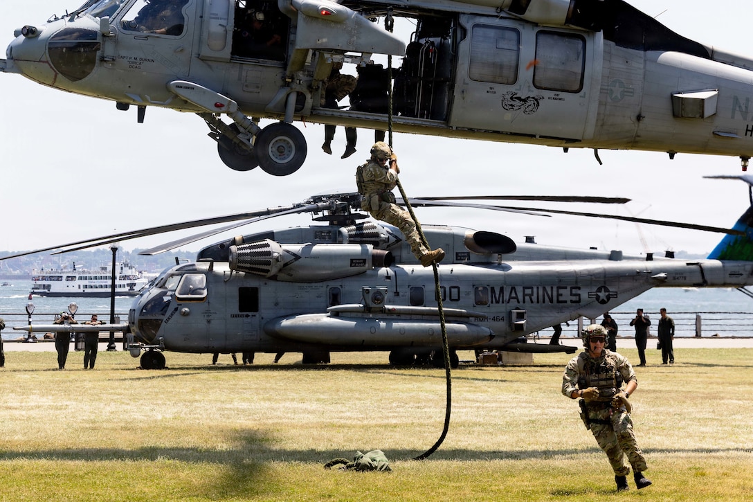 A sailor fast-ropes from a hovering helicopter into a field during the day.