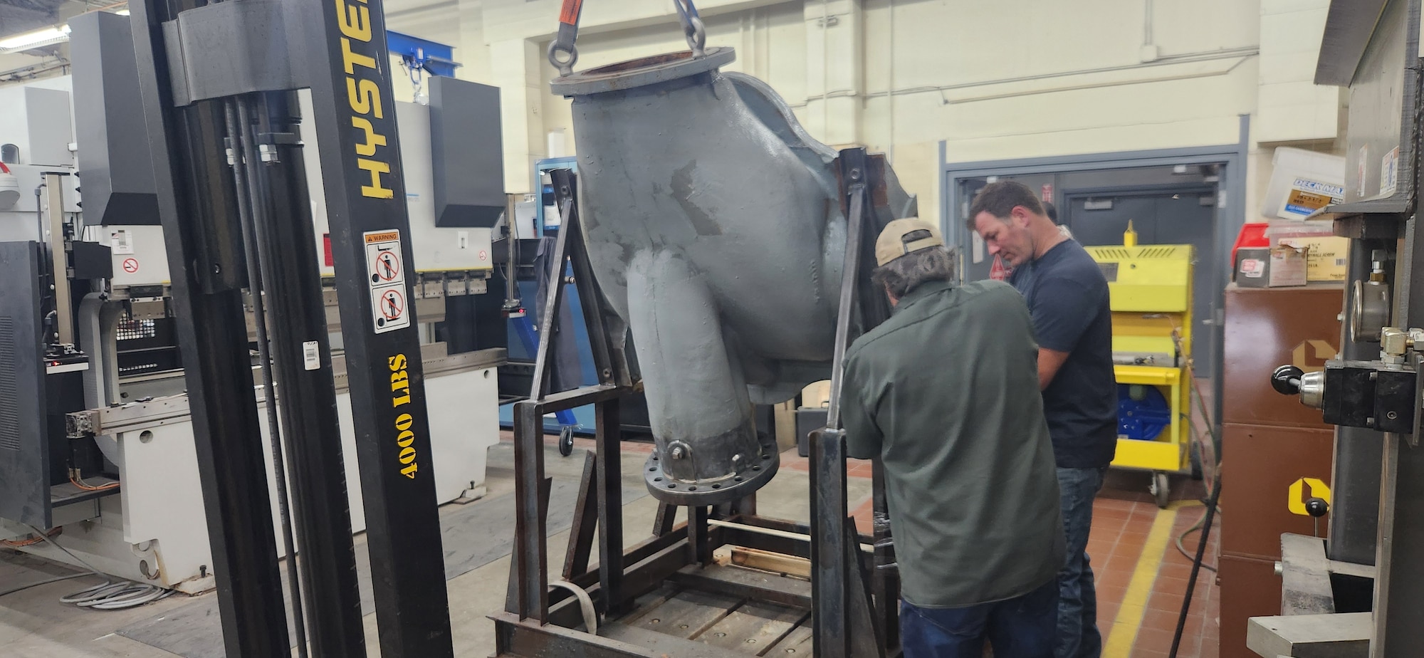 Two people stand and work on metal