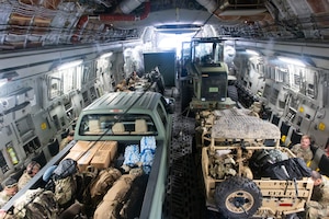 Airmen and vehicles loaded with equipment and supplies sit inside a military aircraft.