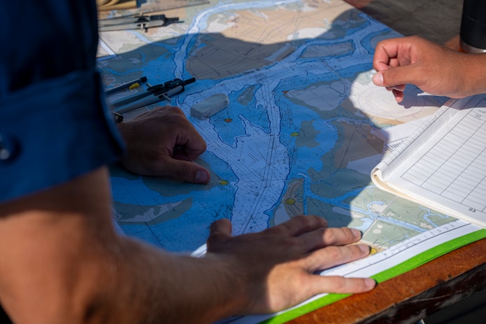 U.S. Coast Guard Academy cadets look at a map on a boat.
