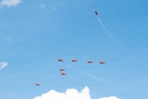 Six red planes fly in a triangle formation, one red plane curves away out of formation and one red plane flies next to the formation.