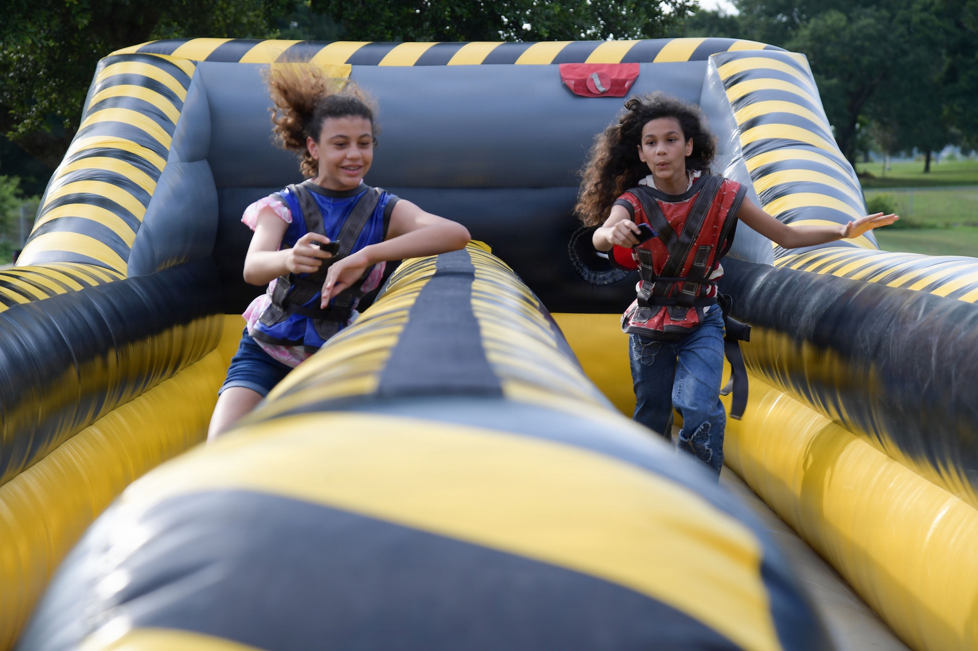 Two girls run down and inflatable obstacle course.