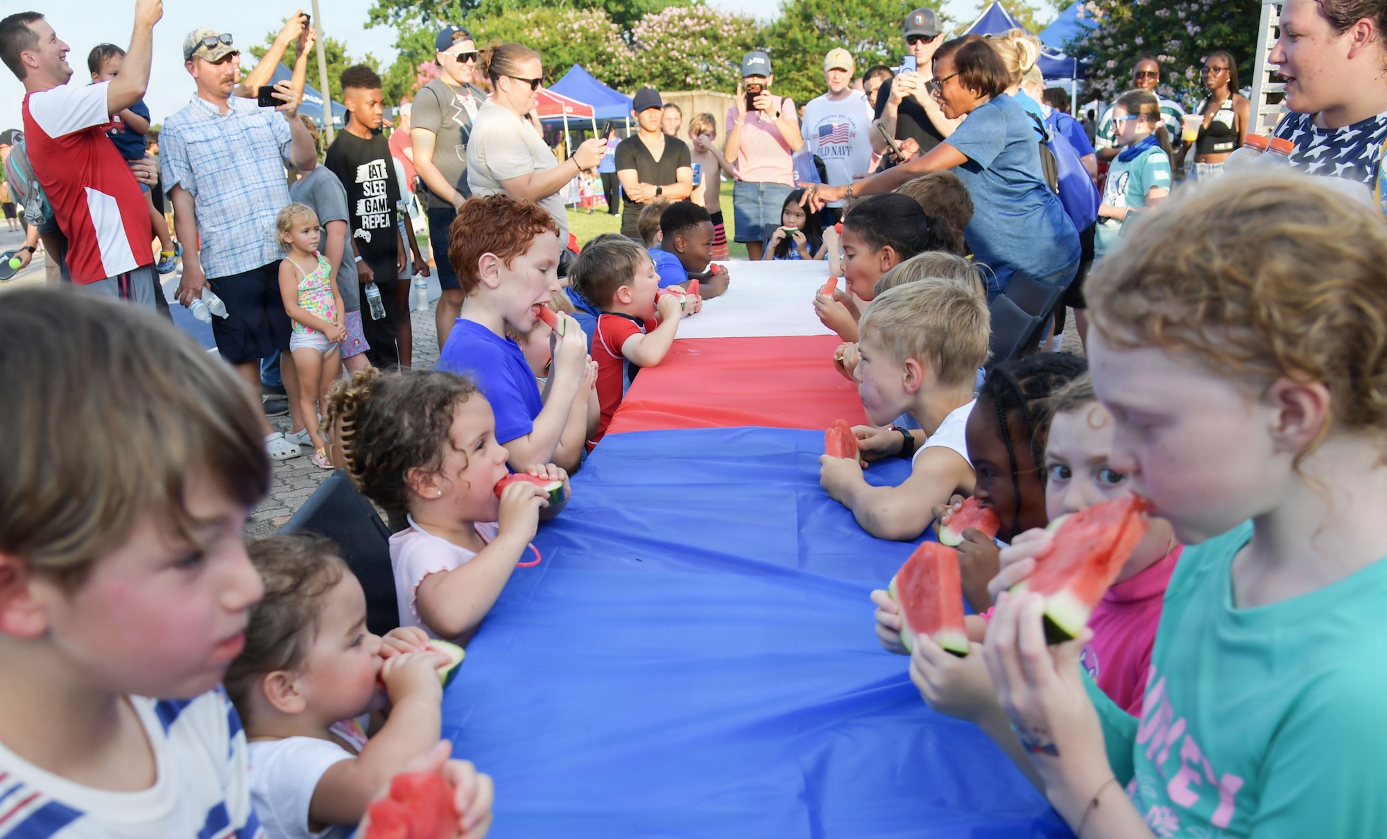 A group of children gather around a table while eating watermelon
