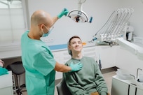 Dentist adjusts the light over a patient sitting in the dentist's chair.