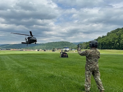 A crew chief assigned to Charlie Company, 131st Aviation Regiment, uses hand-and-arm signals to guide a UH-60M Black Hawk helicopter during sling-load training at Camp Dawson, West Virginia, June 4, 2026.