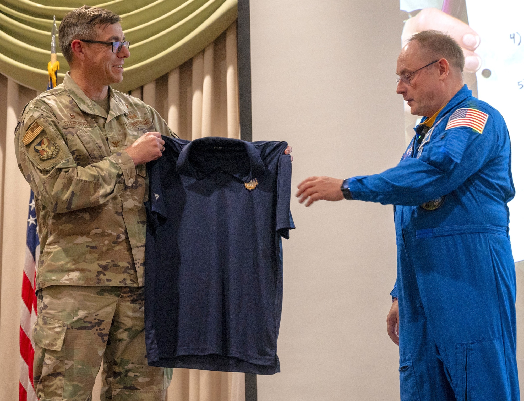 U.S. Air Force Col. Michael Stefanovic, Joint Base McGuire-Dix-Lakehurst and 87th Air Base Wing commander (left), presents retired U.S. Air Force Col. and NASA astronaut Michael Fincke a shirt with the JB MDL emblem during Fincke’s presentation to personnel at JB MDL, N.J., June 22, 2026. Fincke, who joined the NASA astronaut corps in 1996 and has accumulated 549 days in space, brought his decades of military and spaceflight experience to the installation, speaking to both joint base personnel and their children during his visit. (U.S. Air Force photo by Susan Moriarty)
