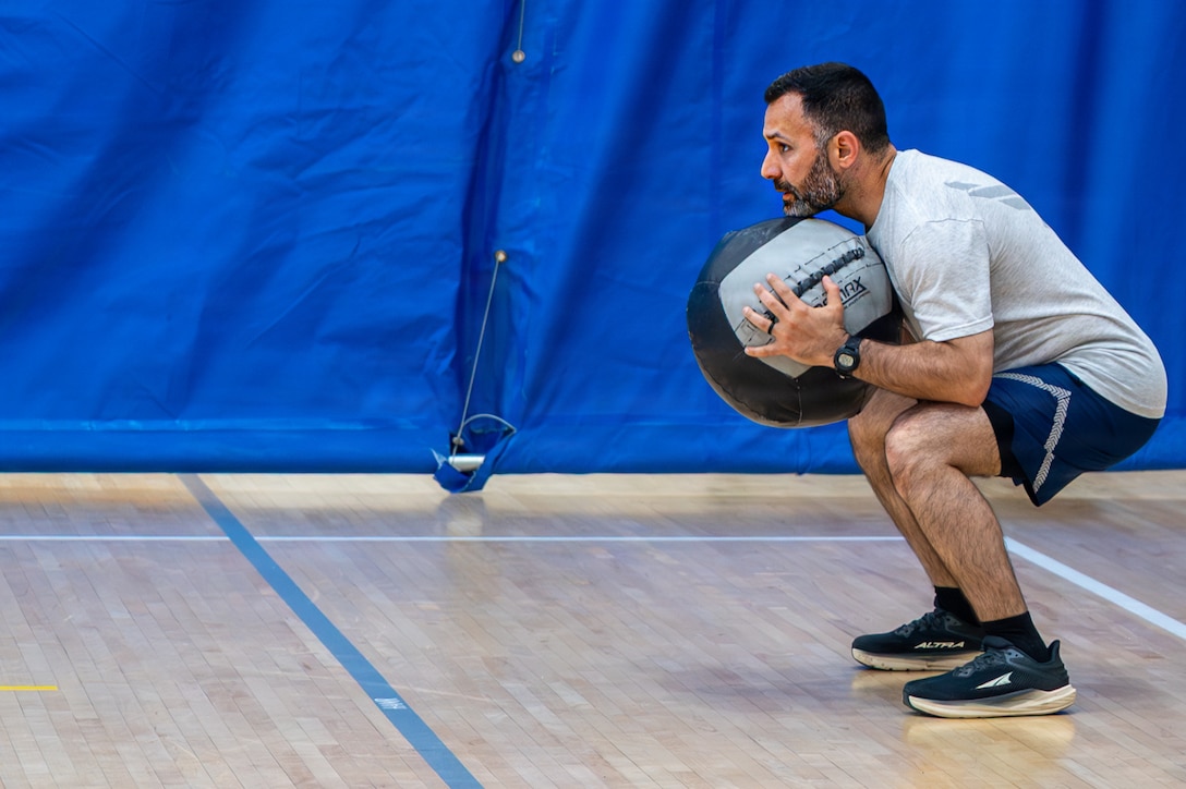 An Airmen squats while holding a weighted ball.