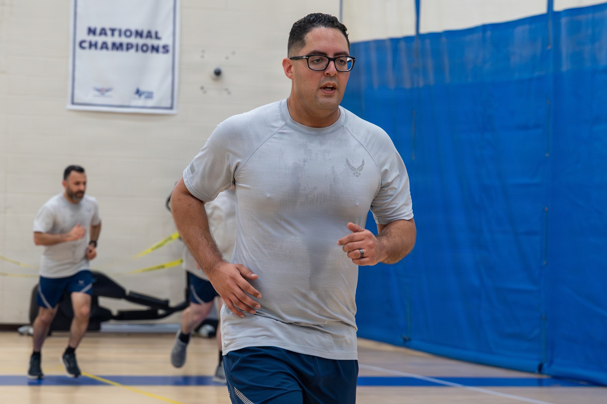 Airmen run in a gym.