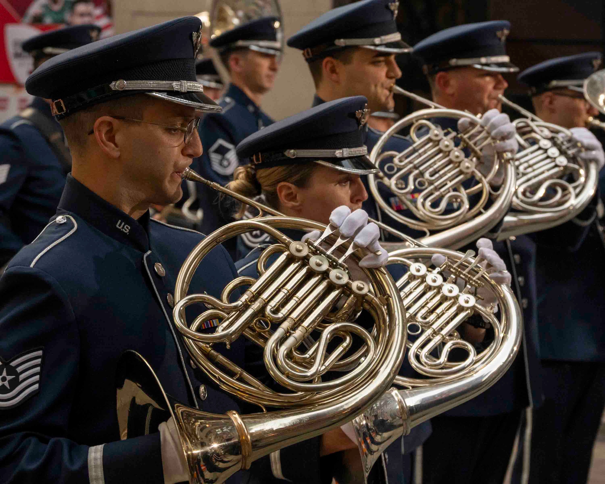 Airmen facing right play French horns in a line, the profile view highlights the overlapping curves of the horns.