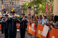 An audience cheers behind orange TODAY Show fences while Airmen play instruments.