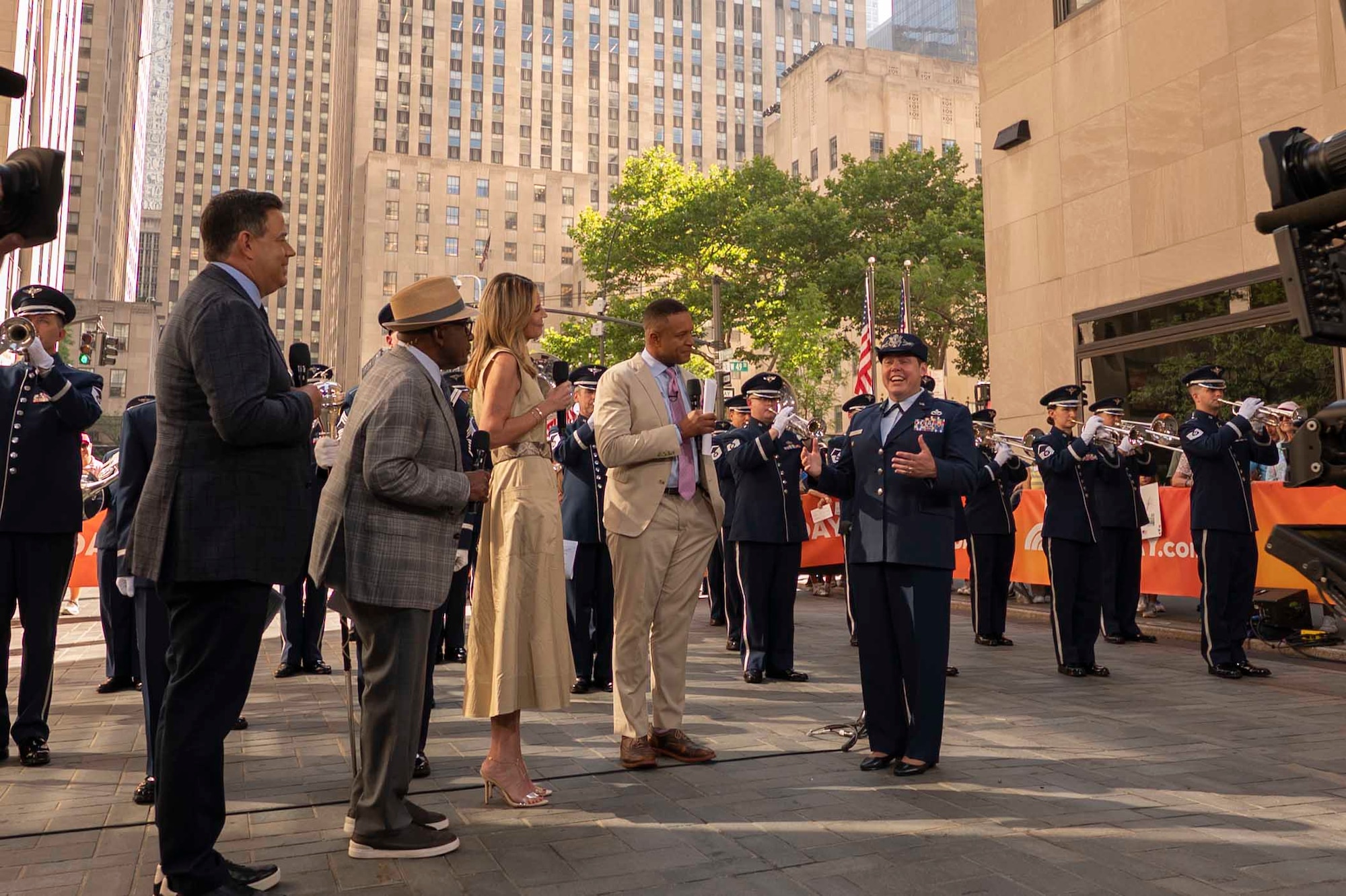 An Airman speaks on the set of the TODAY Show with the Air Force Band and city buildings behind her.