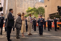 An Airman speaks on the set of the TODAY Show with the Air Force Band and city buildings behind her.