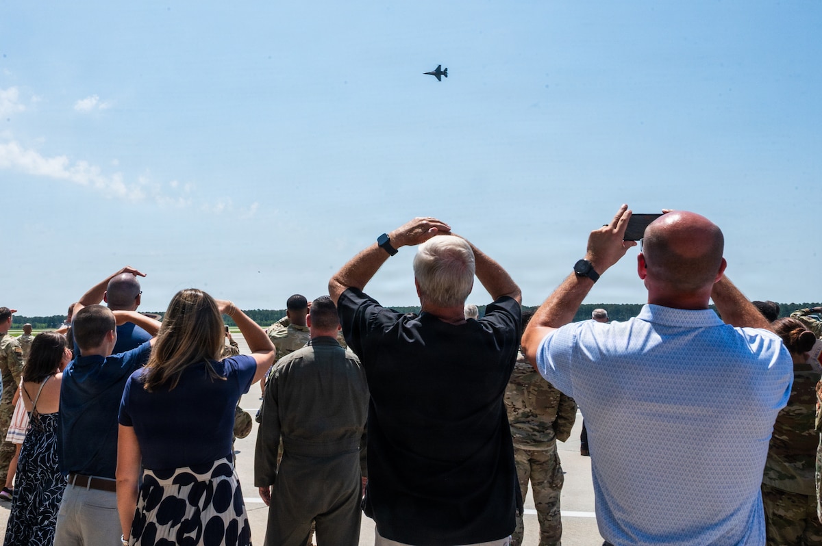 A crowd watches a fighter jet as it flies by them
