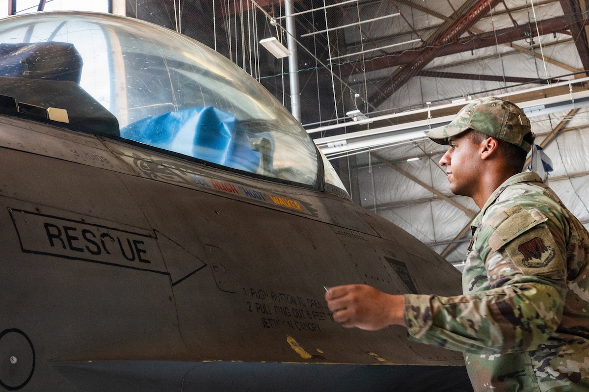 An Airman unveils artwork on a fighter jet