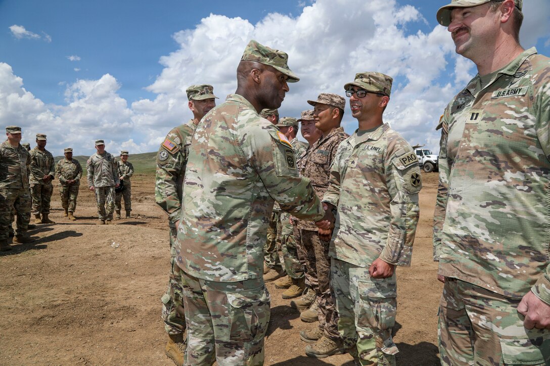 U.S. Army Gen. Xavier T. Brunson, commander of UNC, CFC, and USFK, stands outdoors in military uniform presenting a tri-command challenge coin to Sgt. Joseph Liggio of the 20th Public Affairs Detachment during a handshake at the Five Hills Training Area near Ulaanbaatar, Mongolia, during exercise Khaan Quest 2026.