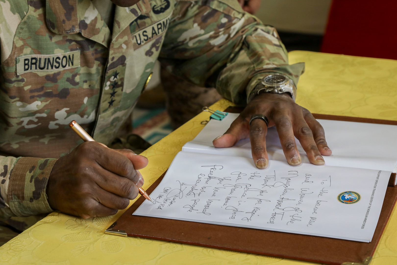 U.S. Army Gen. Xavier T. Brunson, commander of United Nations Command, Combined Forces Command, and U.S. Forces Korea, is shown writing a message in a guestbook or document on a table at the Five Hills Training Area in Mongolia.