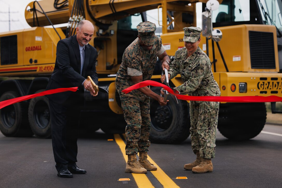 Three people, standing in the center, cut a ribbon during a ceremony with scissors.