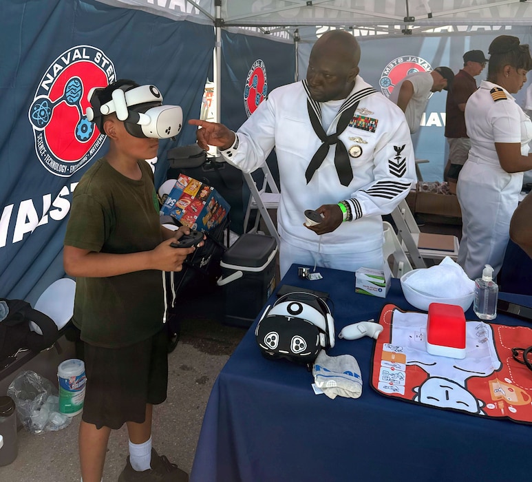 260703-N-N1526-1004 NEW YORK (July 3, 2026) Hospital Corpsman 1st Class Onojakpor Gabriel Ogboru, assigned to Navy Medicine Readiness and Training Command (NMRTC) Fort Belvoir, shows a visitor how to operate a virtual reality simulator for Navy Medicine STEM careers at the U.S. Navy STEM booth at the Intrepid Museum during the International Naval Review 250 (INR 250) in New York, July 3, 2026. For 250 years, the U.S. Navy and Marine Corps stood watch – constant, unabated in mission, faithfully preventing crisis and resolute in defending America’s independence. INR 250 honors the Navy, Marine Corps, and Coast Guard’s enduring role on, under, and above the seas.  (U.S. Navy Capt. Bill Urban)