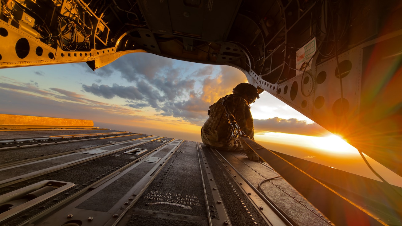 black hawk crew member sitting at the opening of helicopter with the sunset