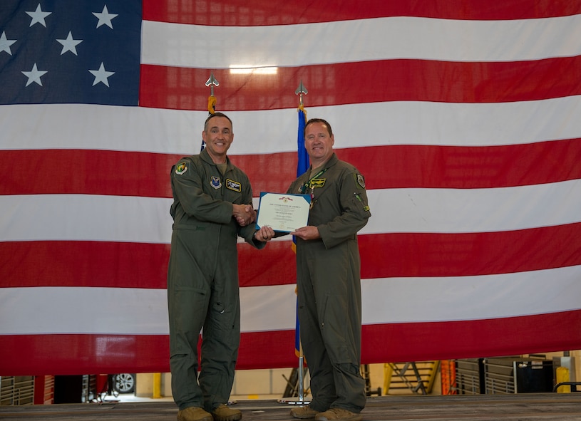 U.S. Air Force Col. John Burrell, 5th Operations Group (OG) outgoing commander, right, receives the legion of Merit certificate from U.S. Air Force Col. Jesse Lamarand, 5th Bomb Wing commander, left, during a change of command ceremony at Minot Air Force Base, North Dakota, July 7, 2026. As the 5th OG commander, Burrell was responsible for leading the operational flying mission of the 5th Bomb Wing.