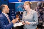 Two people in suits have a conversation in front of a convention floor booth.