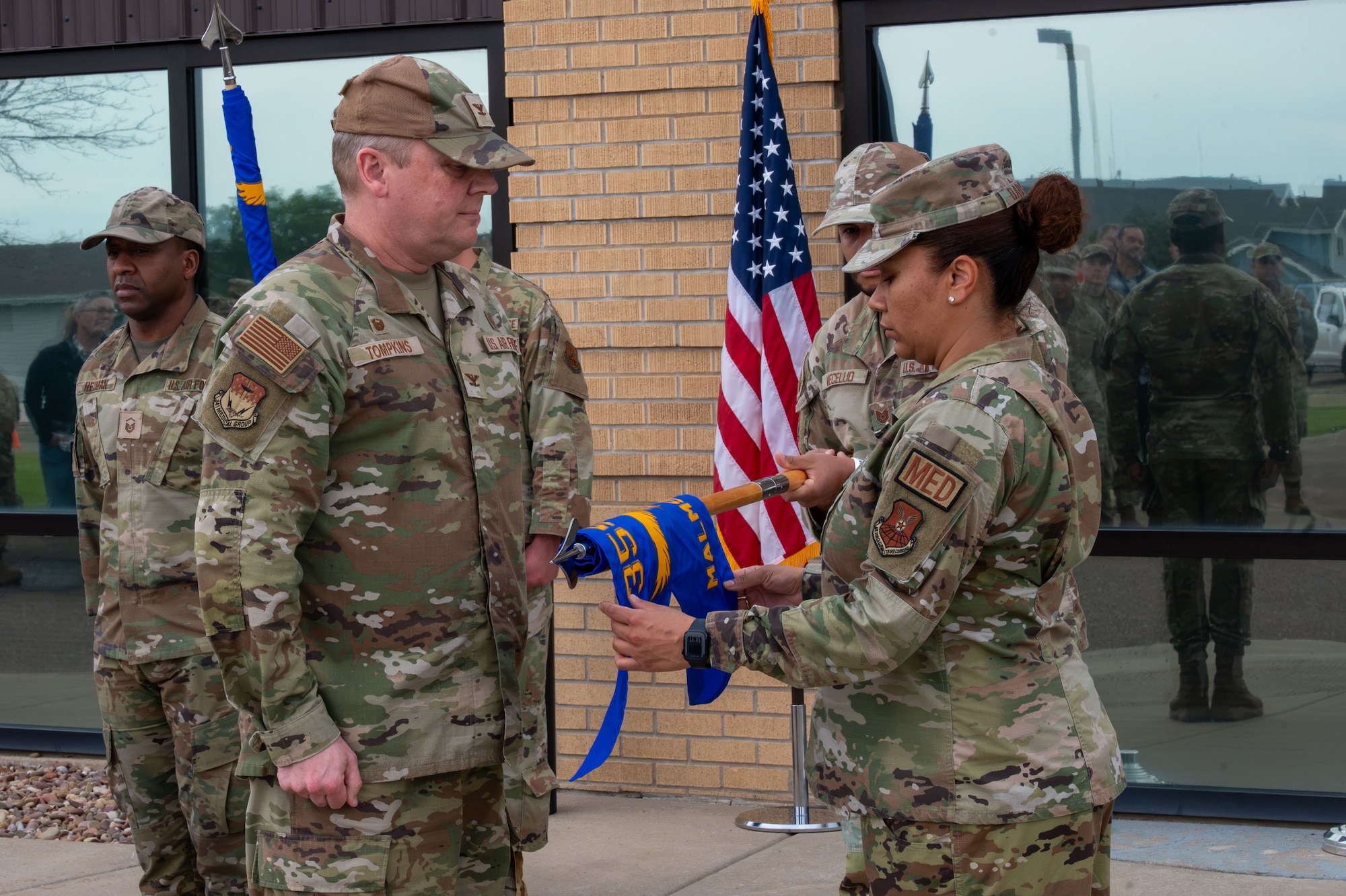 U.S. Air Force Col. Jason Tompkins, Malmstrom Medical Group commander, left, and Master Sgt. Nicole DaGraca, Malmstrom MDG resource management office flight chief, unfurl the new Malmstrom Medical Group guidon during the Air Force Medical Command’s fourth inter-command transfer, at Malmstrom Air Force Base, Montana, June 26, 2026.